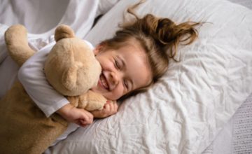 Happy toddler in bed hugging a teddy bear and smiling