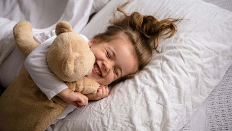 Happy toddler in bed hugging a teddy bear and smiling