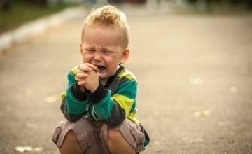 A toddler squats down crying outside on road.