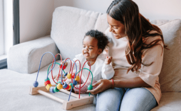 Mother sitting with toddler playing with a toy.