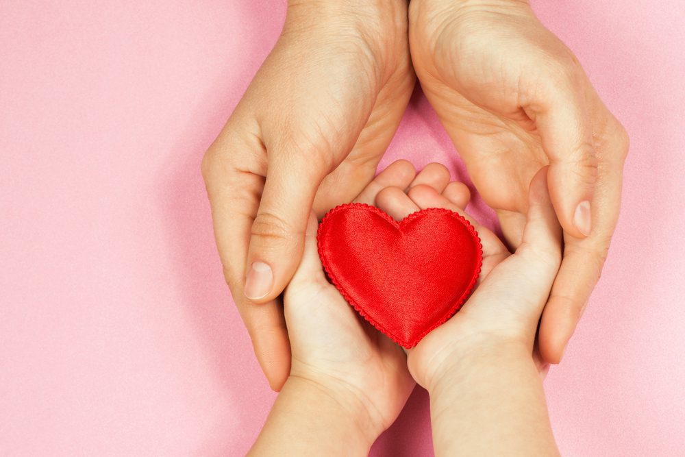 adult hands holding child hands holding a fabric heart