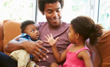 Dad sitting on the couch with two kids, listening to little girl talk