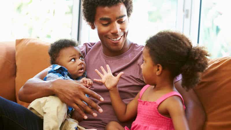 Dad sitting on the couch with two kids, listening to little girl talk