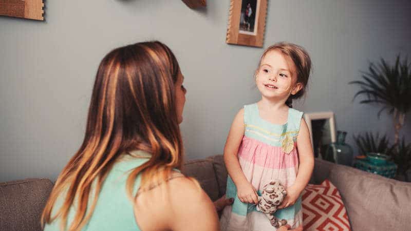 A little girls holds a stuffed toy and looks at mom.