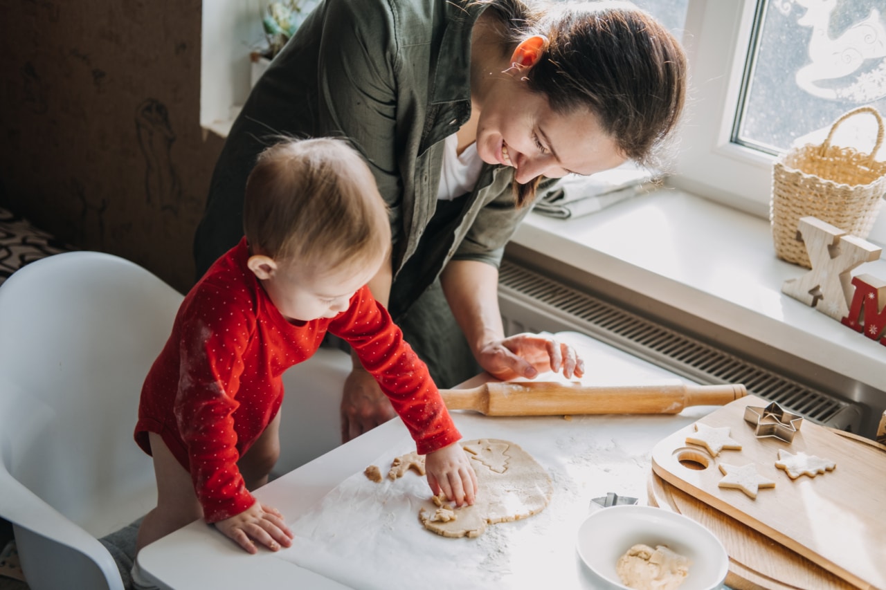 Happy mother and little baby toddler girl making Christmas cookies in home kitchen. Mother and little girl baking Christmas gingerbread pastry for family dinner