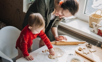 Happy mother and little baby toddler girl making Christmas cookies in home kitchen. Mother and little girl baking Christmas gingerbread pastry for family dinner