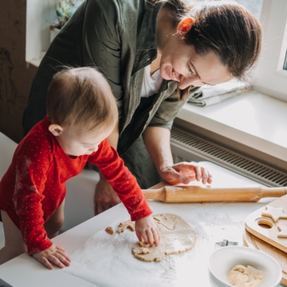 Happy mother and little baby toddler girl making Christmas cookies in home kitchen. Mother and little girl baking Christmas gingerbread pastry for family dinner