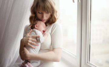 A mother holds a crying baby near window