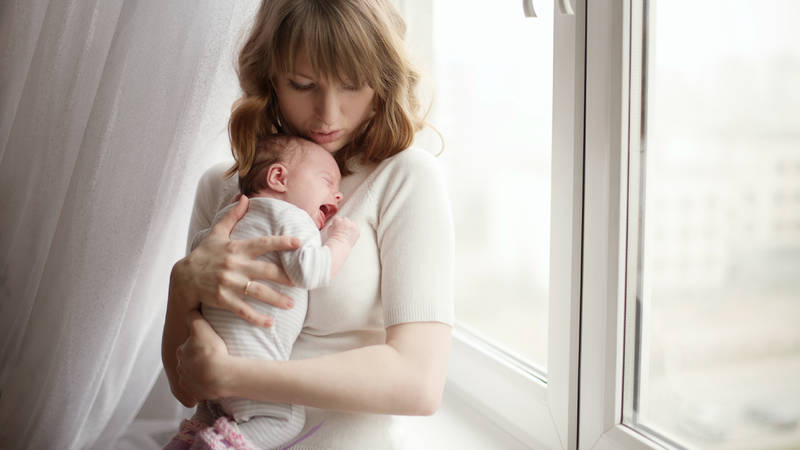 A mother holds a crying baby near window