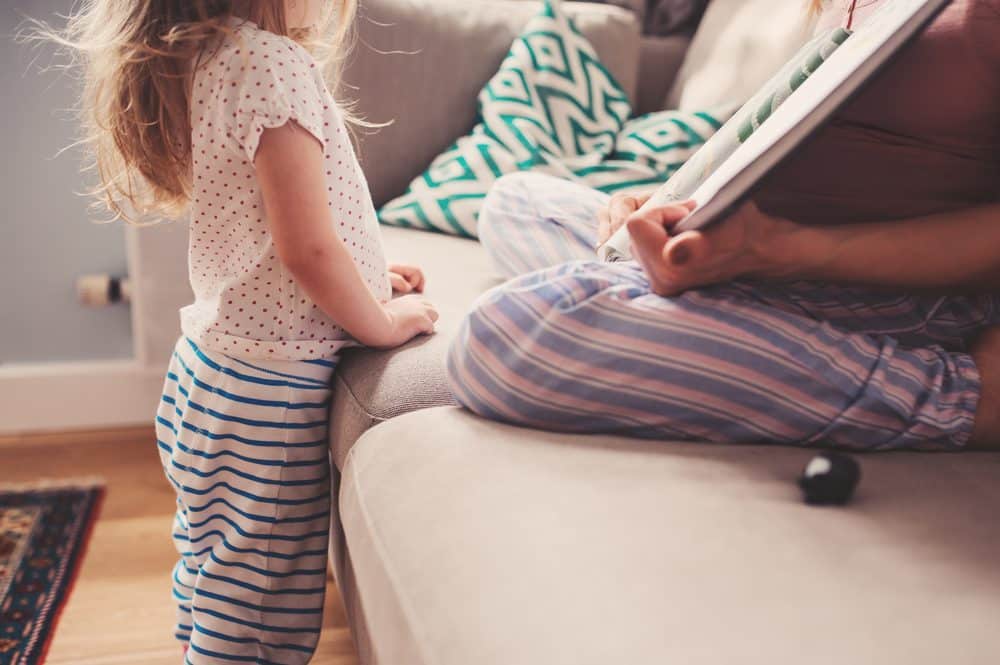 A child stands and listens as an adult reads her a story.