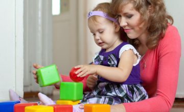 woman holds child playing with blocks