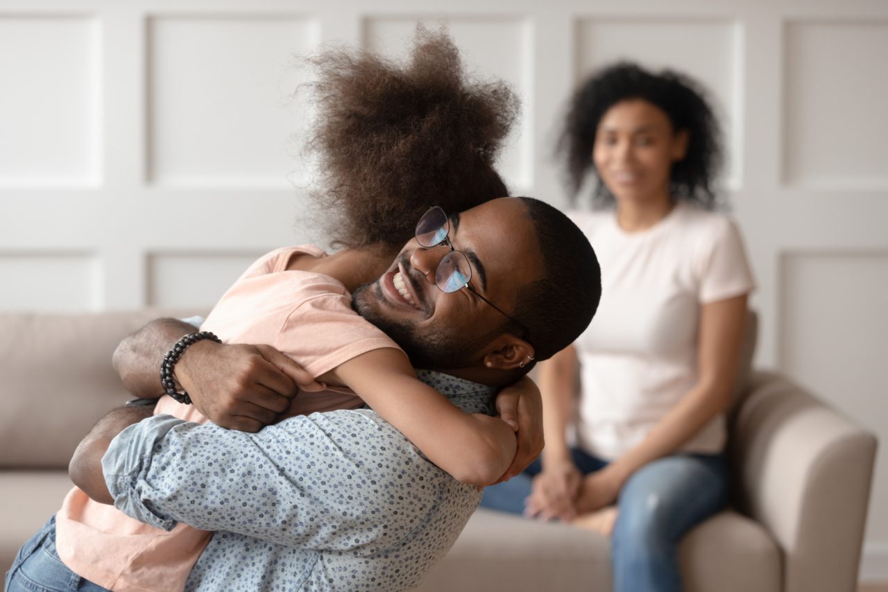 A dad hugs his daughter while her mother looks on behind them.