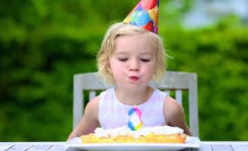 little girl sits at table and blows out birthday candle