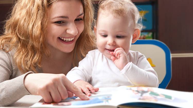 Mother reading a book to a smiling baby
