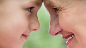A child and grandparent look into each other's eyes while touching foreheads.