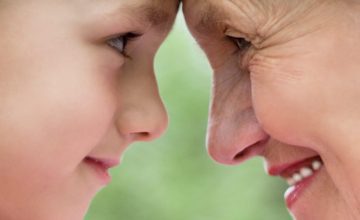 A child and grandparent look into each other's eyes while touching foreheads.