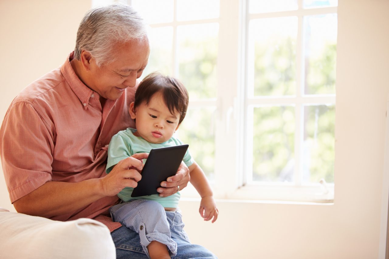 A child looks at a tablet with his grandfather.