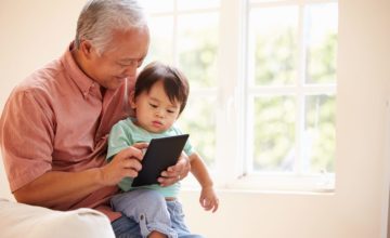 A child looks at a tablet with his grandfather.