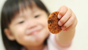 A young child holds up a cookie.
