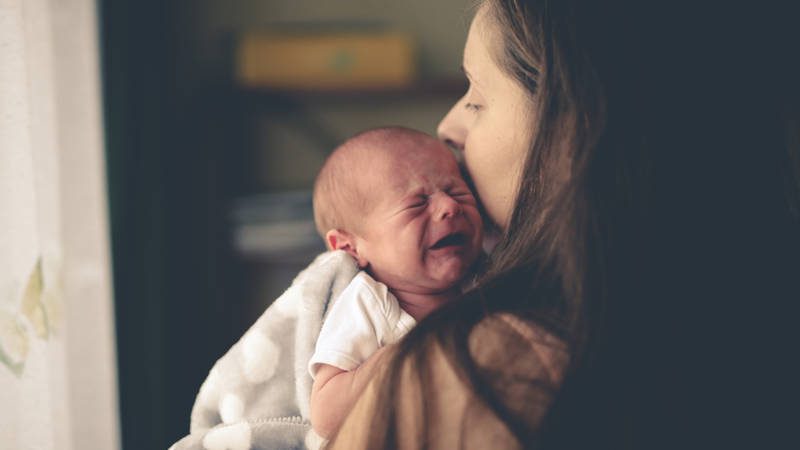 A mom holds a crying baby trying to soothe.