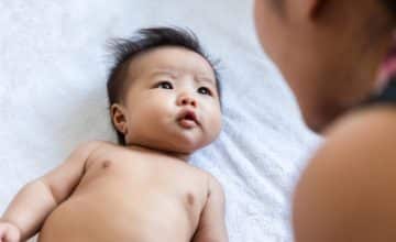 Caregiver looking at baby laying on white background.