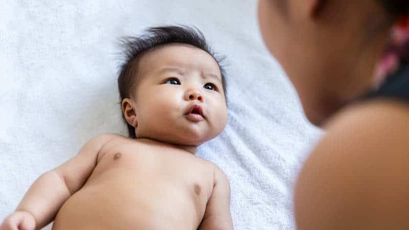 Caregiver looking at baby laying on white background.