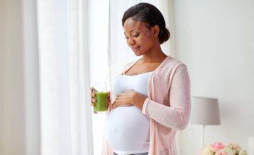 Pregnant mother holding baby bump and green drink