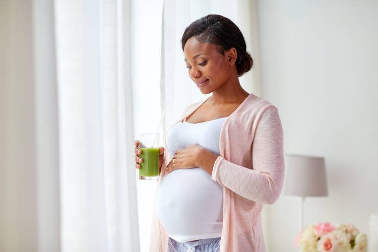 Pregnant mother holding baby bump and green drink