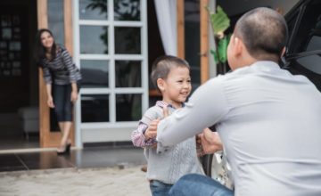 A child is embraced by his father while his mother looks on from a distance.