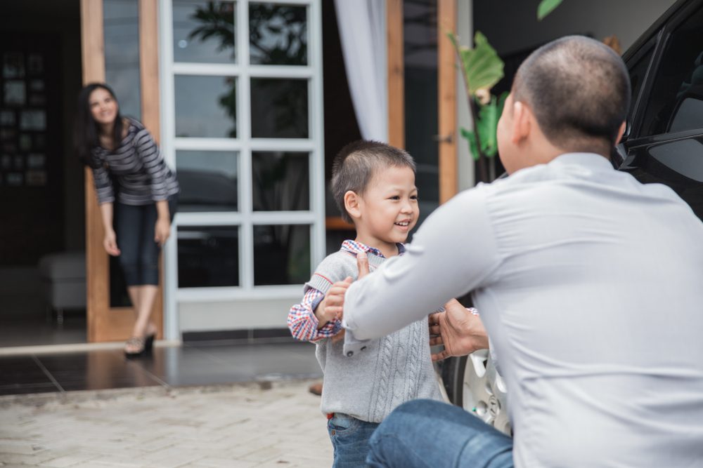 A child is embraced by his father while his mother looks on from a distance.