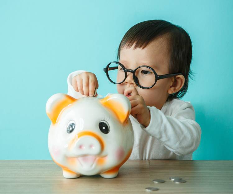 Toddler putting a coin in a piggy bank wearing glasses
