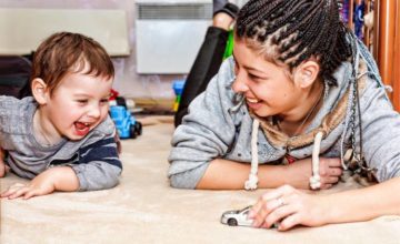 Adult professional laying on floor with smiling toddler