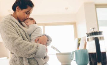 New mother holding baby in arms in kitchen in the morning