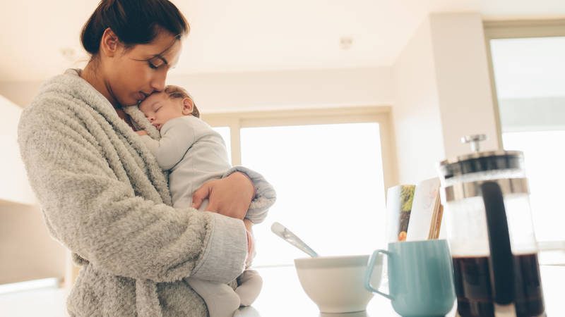 New mother holding baby in arms in kitchen in the morning