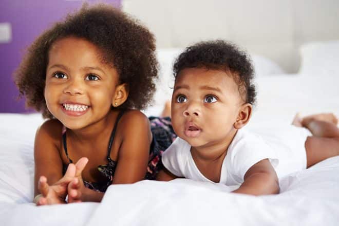 Two children lie on a bed together.