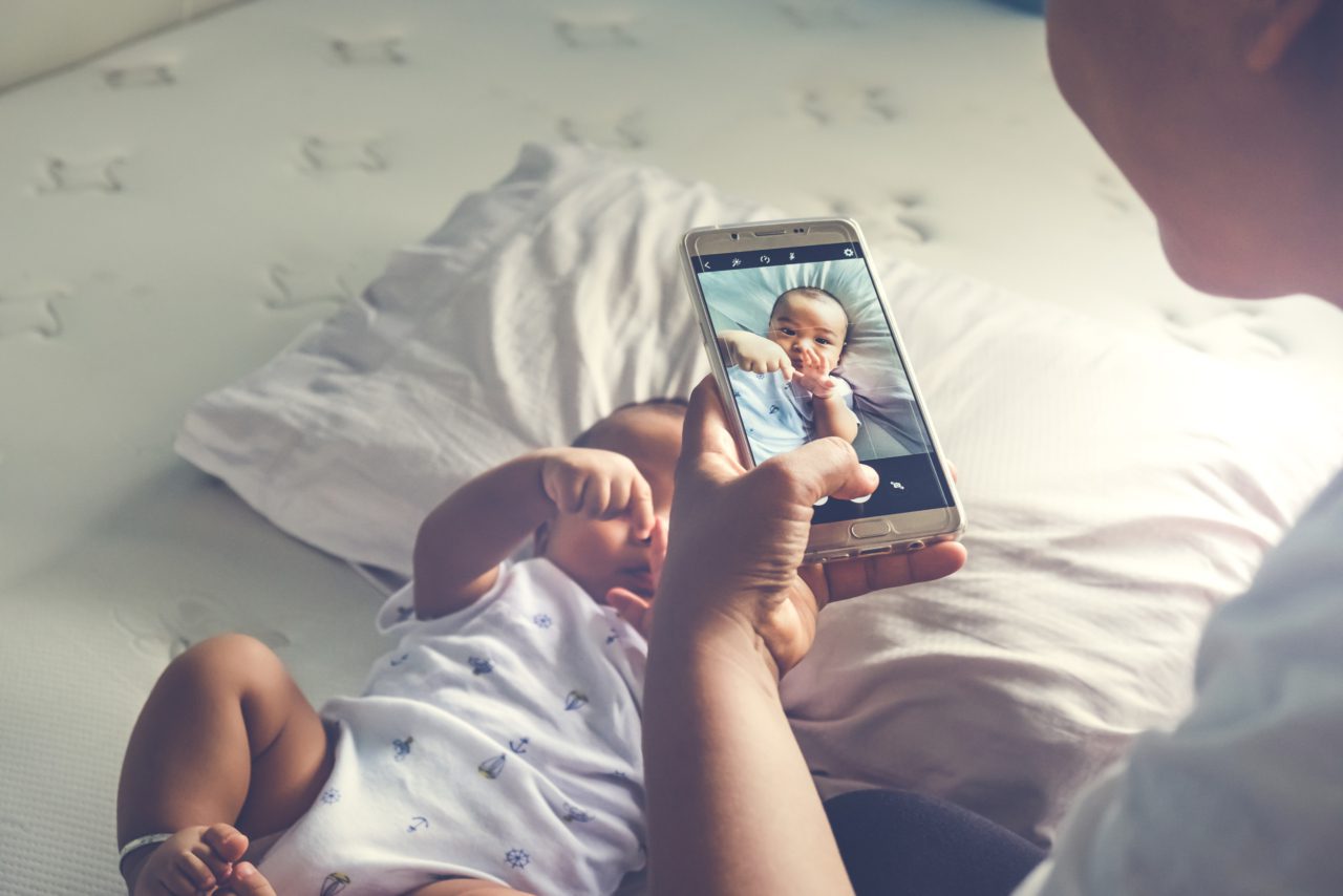 parent takes picture of infant on bed