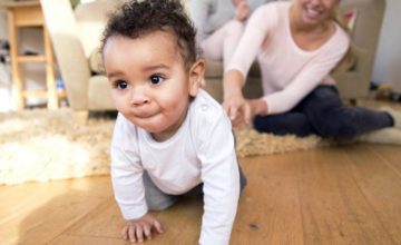A baby crawling across the living room with adults in background