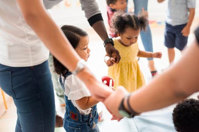 Several children hold hands with adults in a circle.