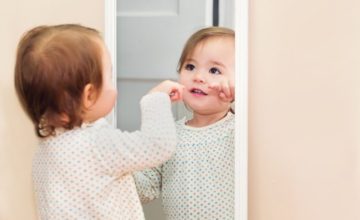 A baby looks at themselves in a mirror.