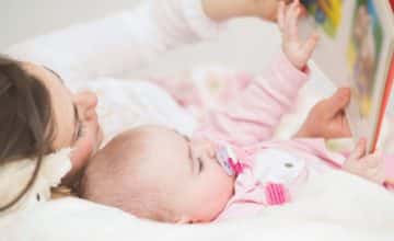 A mother and baby lie in bed looking at a storybook.