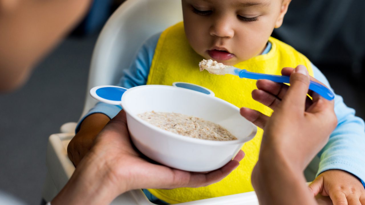 parent feeding toddler oatmeal in highchair