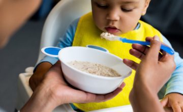 parent feeding toddler oatmeal in highchair