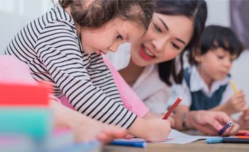 Adult smiling and teaching two toddlers to write