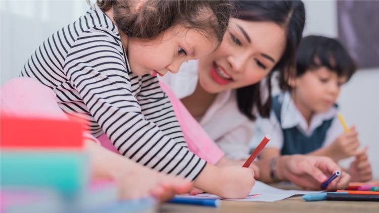 Adult smiling and teaching two toddlers to write