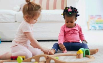 Two girl toddlers playing together on the floor with toys