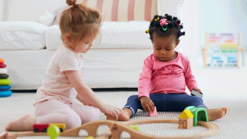 Two girl toddlers playing together on the floor with toys