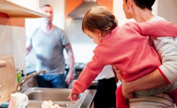 Mother holding baby in arms in kitchen talking to dad in the doorway.