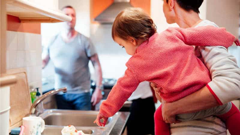 Mother holding baby in arms in kitchen talking to dad in the doorway.