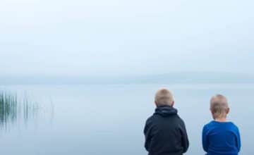 young boys sitting in front of lake