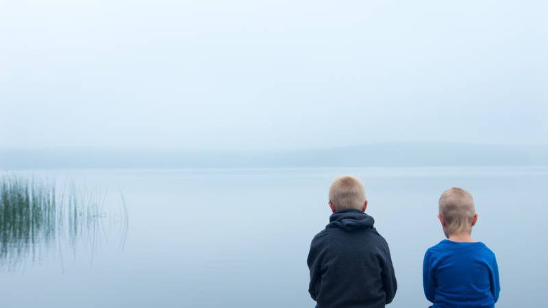 young boys sitting in front of lake